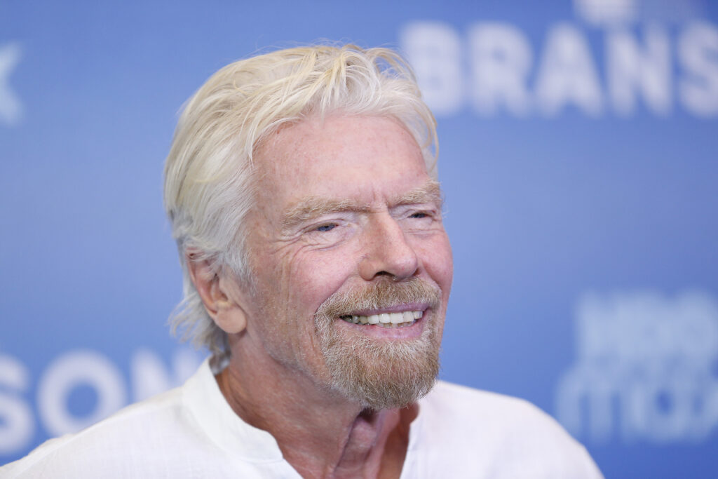 Richard Branson lächelt vor Werbewand