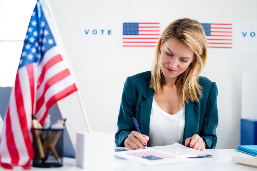 Frau sitzt neben der amerikanischen Flagge an einem Tisch und unterschreibt ein Papier