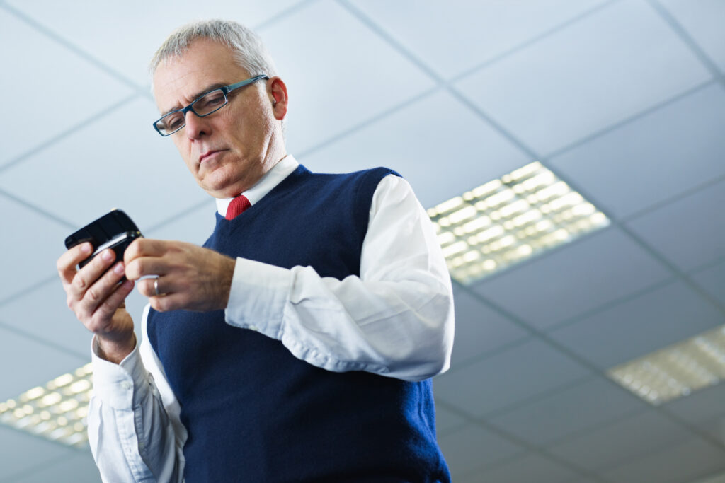 Mann mit Mobiltelefon in der Hand und Brille blickt auf sein Handy