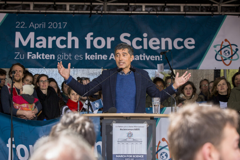 Ranga Yogeshwar spricht vor einem Publikum. Dahinter ein Plakat mit March for Science