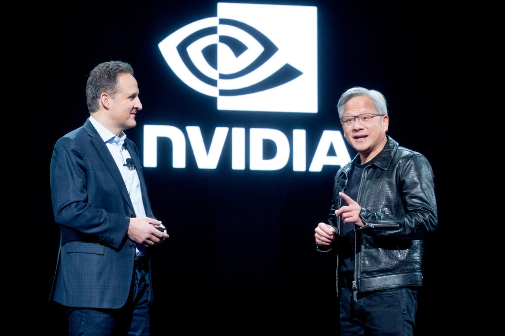 Jensen Huang steht vor dem Logo von Nvidia. neben ihm ein anderer Mann