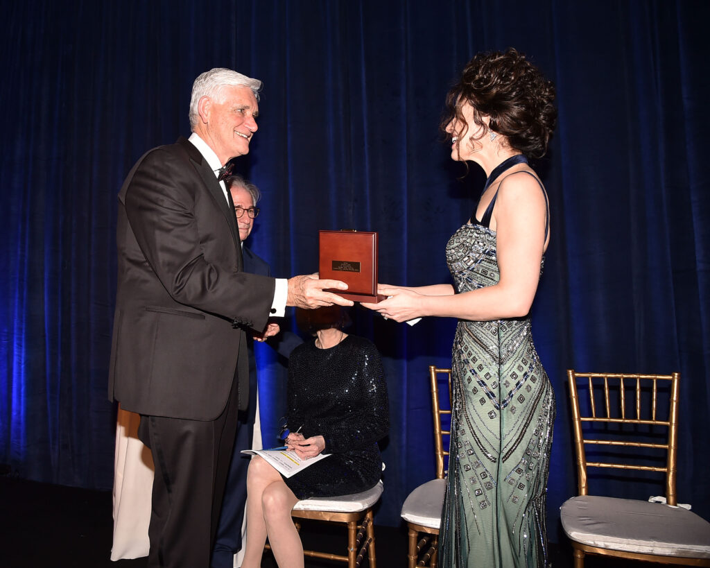 Neri Oxman in Abendkleid bekommt von einem Herren einen Preis überreicht