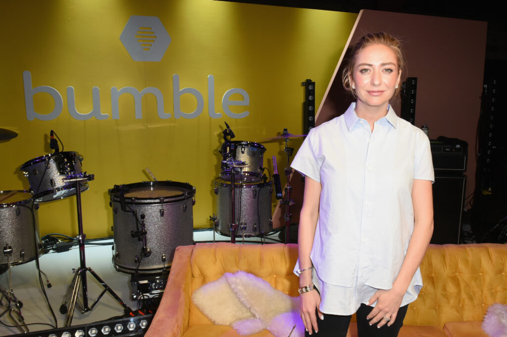 Whitney Wolfe Herd mit weißer Bluse vor einem Schlagzeug und dem Logo von Bumble