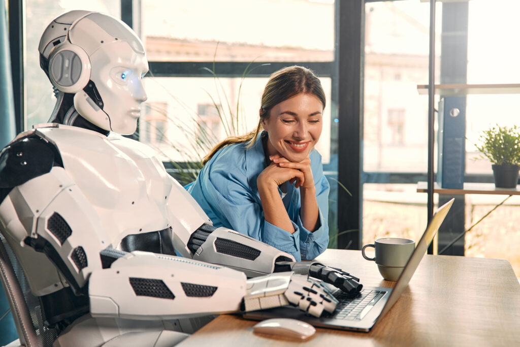 Frau sitzt neben einem Roboter an einem Tisch