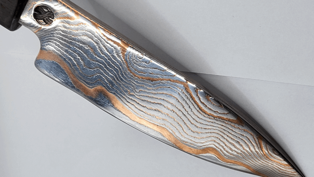 Ein handgefertigtes Damastmesser von Damastique, geschmiedet von Thomas Rath, zeigt das kunstvolle Muster der Damasttechnik.